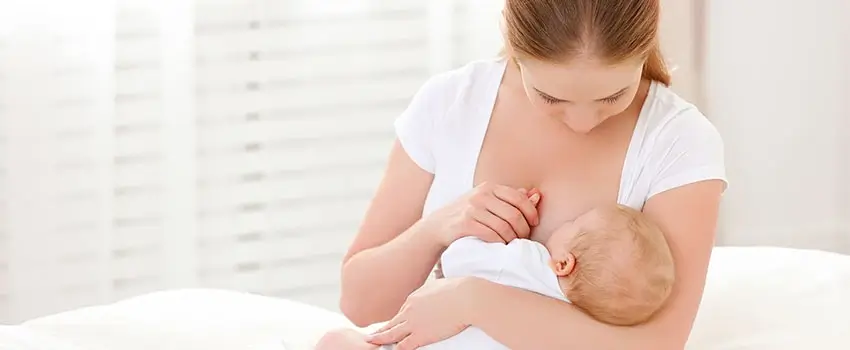 A close-up of a mother in a white t-shirt breastfeeding her child.
