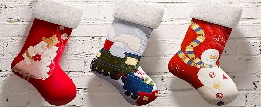 A close-up of three Christmas socks hanging against a white brick wall.