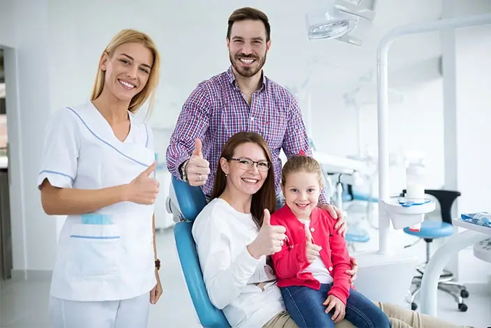 A full shot of a family and a dentist inside a dental clinic doing a thumbs-up gesture.