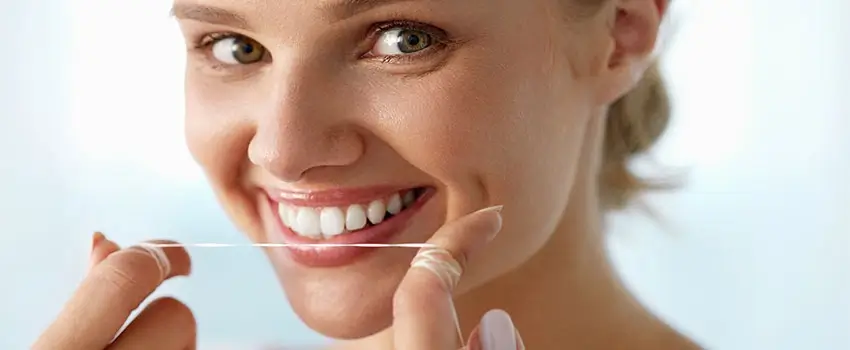 A close-up of a smiling woman holding dental floss near his mouth.