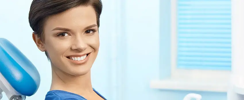 A close-up of a smiling, short-haired woman sitting on an Orthodontic chair.