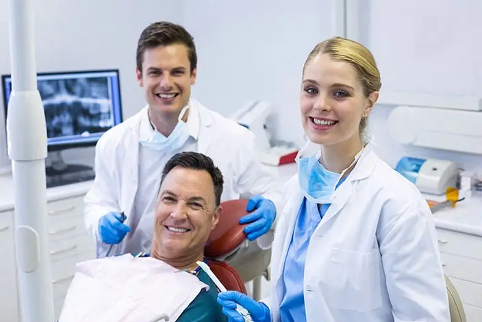 A close-up  of two smiling dentists and a patient lying on an Orthodontic chair inside a dental clinic.