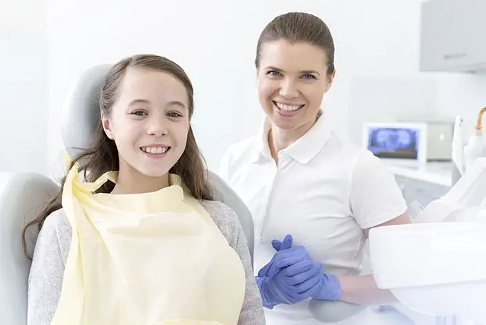 A close-up of a girl patient sitting on an Orthodontic chair with a dental assistant smiling beside her inside a dental clinic.