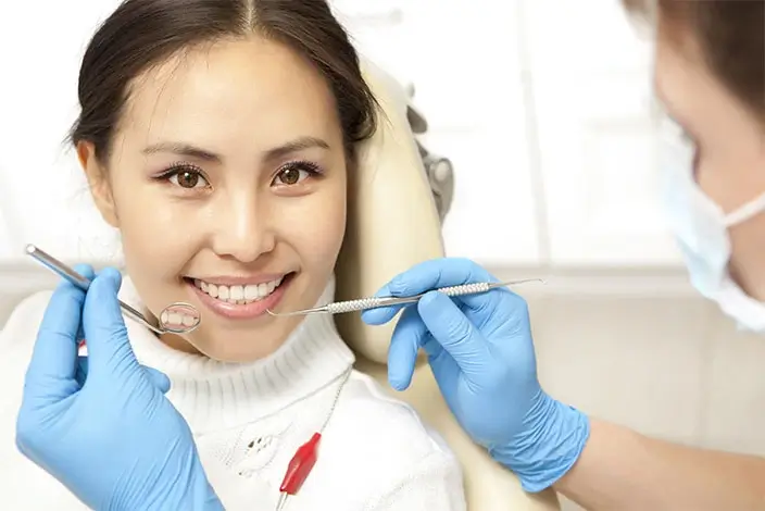A close-up of a smiling patient and a dentist holding a dental instrument inside a dental clinic.