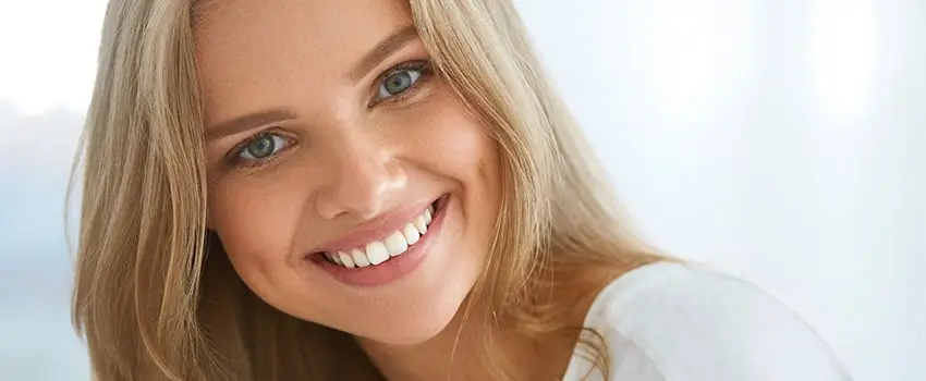 A close-up of a smiling blond woman with an ash-grey eye color.